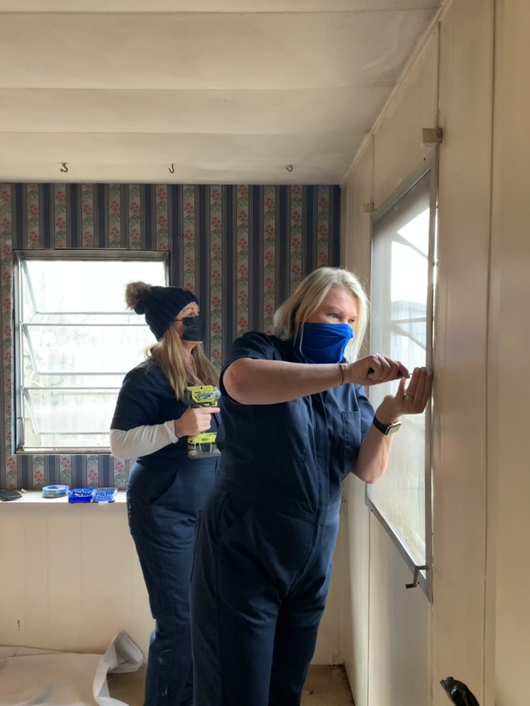 Volunteers in navy jumpsuits installing a bedroom window frame during a one-day Room Redux of Georgia transformation.