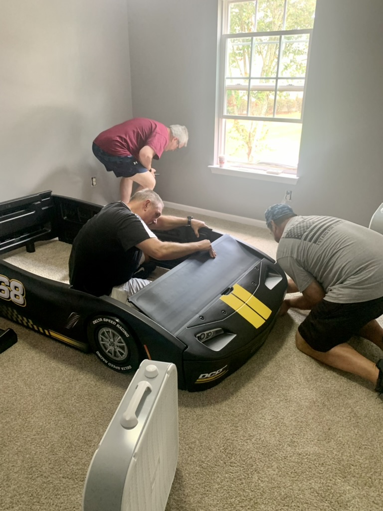 RRGA volunteers assembling a car-shaped bed during a room transformation.